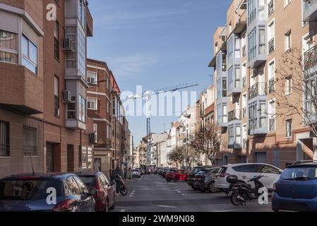 Eine urbane Straße mit modernen Flachbauten und batteriegeparkten Fahrzeugen und einem großen Baukran im Hintergrund Stockfoto