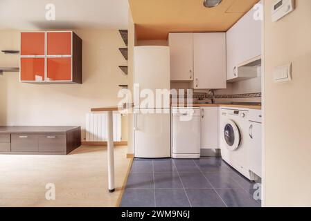 Möblierte Küche, die zum Wohnzimmer im Loft-Stil eines Wohnhauses mit weißen Möbeln und einem kleinen Inseltisch mit weißem Metallle führt Stockfoto