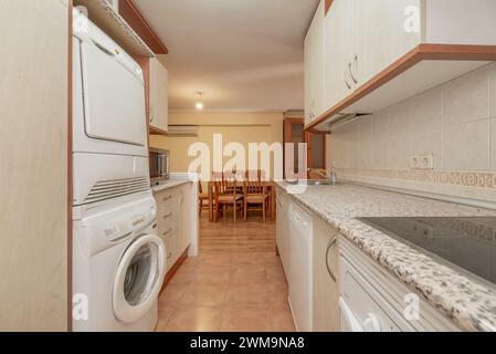 Möblierte Küche offen zum Esszimmer mit weißen Möbeln, ähnlich rosa Granitarbeitsfläche, Waschmaschine und Trockner Turm in einem Loft-Stil Haus mit offenem Stockfoto