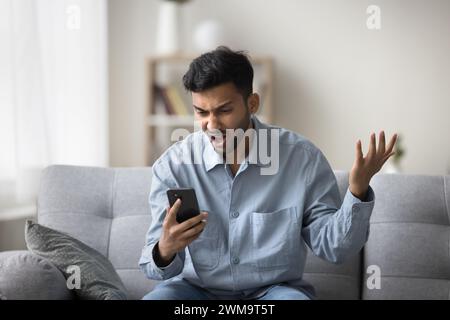Indianer starrt auf den Smartphone-Bildschirm mit wütendem Gesichtsausdruck Stockfoto