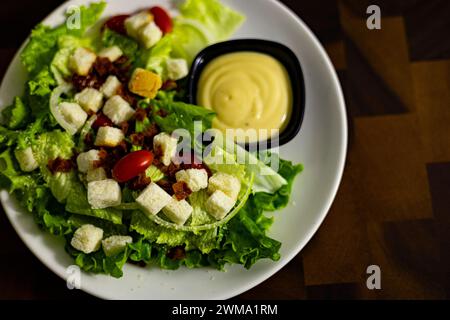 Caesar Salat mit Croutons, Wachteleiern, Kirschtomaten und gegrilltem Huhn auf weißem Teller auf dunklem Holztisch Stockfoto