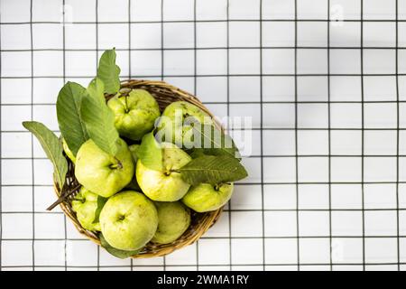 Blick von oben auf eine frische grüne, rohe Guave. Früchte mit hellgrüner Rinde und weißem Fruchtfleisch, süß, knusprig in einem Bambuskorb isoliert auf weißem Hintergrund Stockfoto