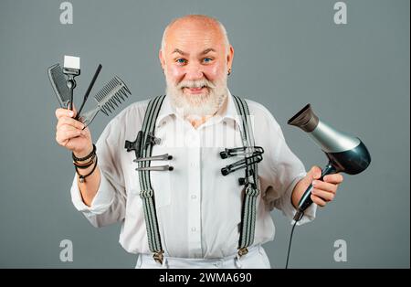 Mann mittleren Alters, Friseur hält Friseur Ausrüstungen, isoliert auf grauem Hintergrund. Friseurladen Barbershop Konzept. Haarbehandlung für Männer. Stockfoto
