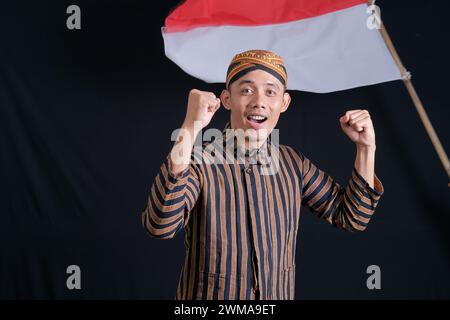 Junger Mann mit indonesischer Nationalflagge, der den Monat der Unabhängigkeit auf schwarzem Hintergrund begrüßt Stockfoto