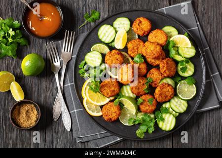 Gebratene Reispasteten, Reis Tiki, indischer Stil auf schwarzem Teller serviert mit Gurke, Zitrone, Limettenscheiben und süßer Chili-Sauce auf dunklem Holztisch, flach Stockfoto