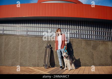 Hipster-Mann, der mit einem Hund an der Leine Skateboard fährt und den Sommer genießt Stockfoto