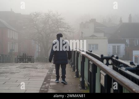 Windsor, Berkshire, Großbritannien. Februar 2024. Ein Fußgänger überquert die Windsor Bridge im Nebel. Heute war es ein nebeliger Morgen in Windsor, Berkshire, aber der Sonnenschein verbrannte schnell den Nebel und Nebel. Quelle: Maureen McLean/Alamy Live News Stockfoto