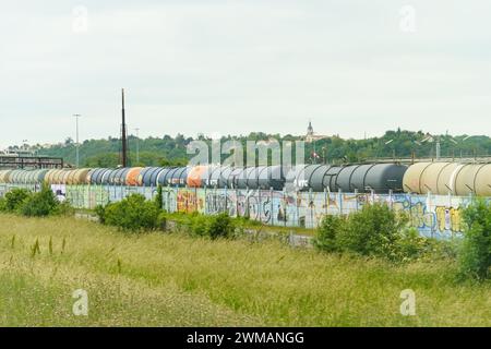 Lyon, Frankreich - 16. Mai 2023: Ein langer Güterzug steht an einem bewölkten Tag auf den Gleisen, im Vordergrund befindet sich ein mit hellem Graffit bedeckter Zaun Stockfoto