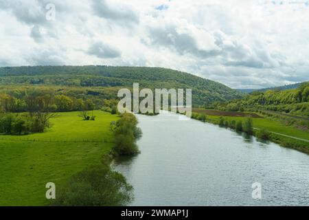 Ein ruhiger Fluss schlängelt sich durch ein lebhaftes grünes Tal, umgeben von sanften Hügeln unter einem teilweise bewölkten Himmel, was auf den frühen Frühling oder Herbst hindeutet. Das u Stockfoto