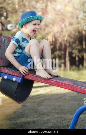 Ein kleiner Junge auf einer Balance, der hochgehoben wird, ist sehr glücklich und lacht. Stockfoto