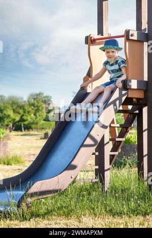 Kinder spielen auf dem Spielplatz im Freien. Aktives Kind auf farbenfroher Rutsche. Gesunde Sommeraktivität für Kinder. Kleiner Junge klettert draußen. Wunderschöne Summe Stockfoto