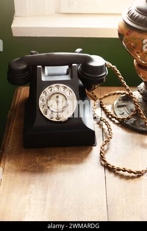 Schwarzes, 1940er Jahre altes Bakelittelefon auf einem Holzschreibtisch in der Nähe des Fensters, brauner Tisch als Hintergrund, der Platz zum Kopieren nach unten bietet. Stockfoto