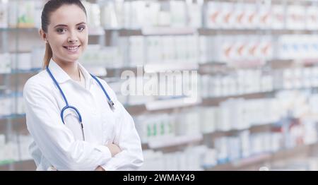 Junge Apothekerin posiert und lächelt vor der Kamera, Apothekenregale im Hintergrund Stockfoto
