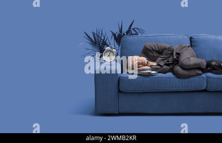 Geschäftsmann, der auf einer Couch schläft, und der Wecker mit zwei Glocken klingelt Stockfoto