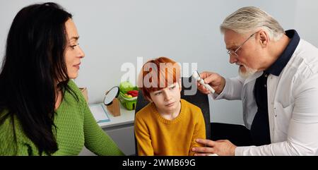 Gutaussehender Junge mit seiner Mutter beim Hörtest, Audiologe mit otoskopprüfendem Ohr des Kindes Stockfoto