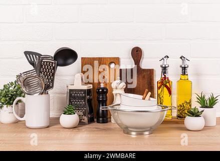 Eine Vielzahl von Küchenutensilien aus Holz und Metall auf einer Holzarbeitsfläche. Glasflaschen mit Öl in einem Holzkoffer. Stilvoller Aufbewahrungsbereich. Stockfoto