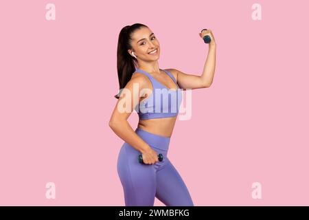 Fröhliche junge Frau, die Gewichte in sportlicher Ausrüstung hebt Stockfoto