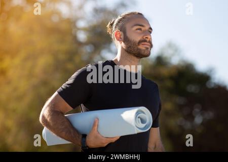 Europäischer Mann in Aktivkleidung hält Yoga-Matte beim Workout im Freien Stockfoto
