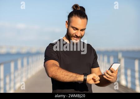 Sportlicher Kerl, der den Puls auf Fitness-Tracker überprüft, der ein Smartphone im Freien hält Stockfoto