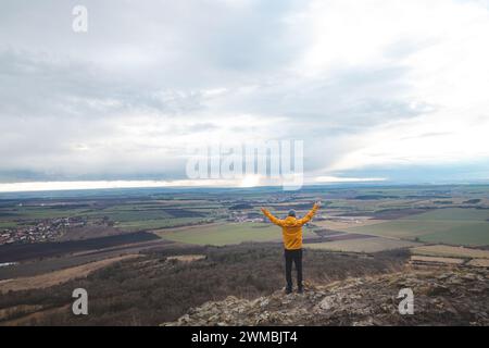 Der Reisende in einer gelben Jacke steht oben auf dem Mount Rip und hebt seine Arme über den Kopf. Erfolg erzielen. Erkunden Sie das tschechische Land. Stockfoto