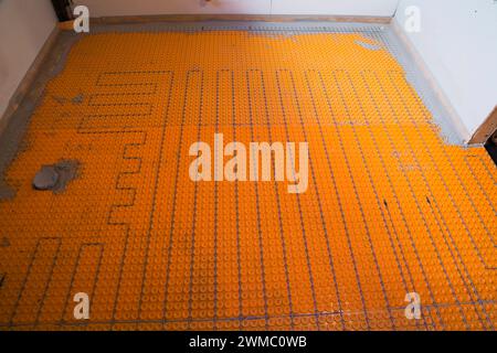 Elektrische Fußbodenheizungen und Temperatursensoren sowie Abflussrohr für die Toilette im unfertigen Waschraum im Untergeschoss eines Bungalows. Stockfoto
