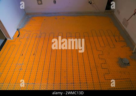 Elektrische Fußbodenheizungen und Sensoren sowie Abflussrohr für die Toilette im unfertigen Waschraum im Untergeschoss eines Bungalows. Stockfoto