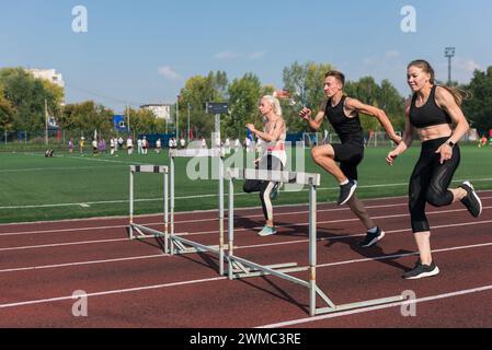 Zwei AthletInnen, Frau und Mann, die im Freien im Stadion Hürden laufen Stockfoto