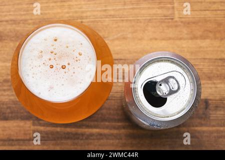 Blick von oben auf Glas gefüllt mit einem goldenen Bier mit einer offenen Bierdose mit Kondenswasser gegen rustikalen Holztisch Stockfoto