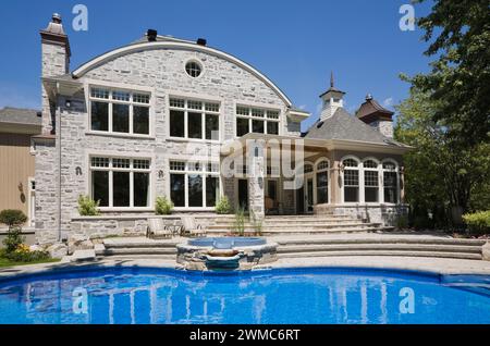 In-Ground Swimmingpool im Hinterhof eines luxuriösen zweistöckigen Natursteinhauses im Sommer. Stockfoto