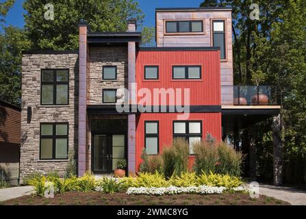 Modernes zweistöckiges Haus aus Naturstein im Cube-Stil mit rötlich gebeizten Holzdielen und Kupfer plus angelegtem Vorhof im Sommer. Stockfoto