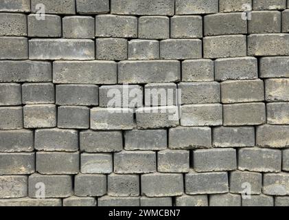 Die Oberfläche einer Mauer oder eines Zauns, die mit grauen Ziegeln ausgekleidet ist. Pflasterplatten aus grauen Blöcken von flacher Form. Straßenpflaster im Stadtpark. Parkweg-Materialien Stockfoto