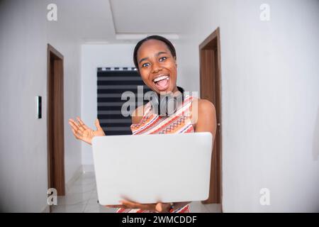 Bild einer fröhlichen jungen Frau, die mit einem Laptop steht. Die Kamera sieht aus. Stockfoto