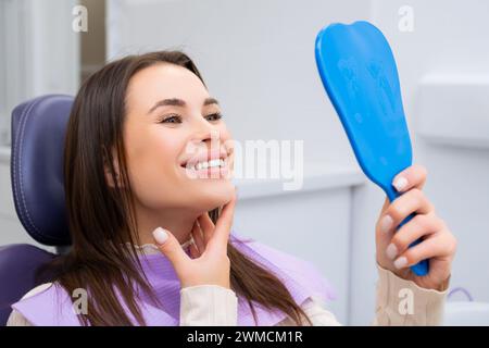 Die Patientin schaut zufrieden in den Spiegel, während sie im Zahnarztstuhl im medizinischen Zentrum sitzt Stockfoto