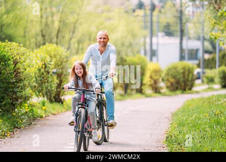 Porträts lächelnder Vater mit Tochter während des Sommerfahrens im Freien. Sie genießen die Zusammengehörigkeit im Sommer-Stadtpark. Glückliche Eltern und Chi Stockfoto