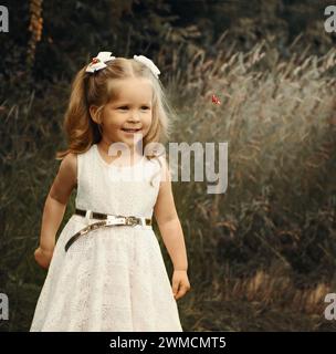 Das kleine lächelnde Mädchen sieht im Sommer Marienkäfer in der Natur an. Stockfoto