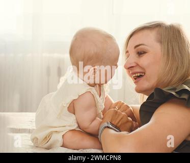 Die junge Mutter spielt, kocht und lacht mit ihrem Baby an einem sonnigen Tag zu Hause Stockfoto