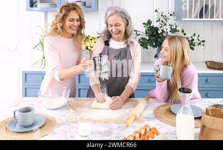 Drei Generationen von Frauen versammeln sich in der gemütlichen Küche, machen und Rollen Teig zusammen mit Lächeln und Lachen aus. Großmutter unterrichtet ihre Tochter und g Stockfoto