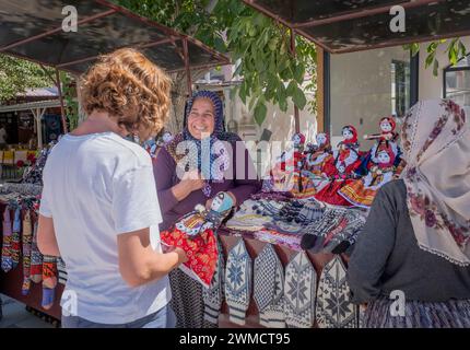 Ein Tourist kauft eine handgefertigte Stoffpuppe in typischen kappadokischen Kleidern von einer türkischen Frau, die mit ihr ein Lächeln waagerecht verhandelt Stockfoto