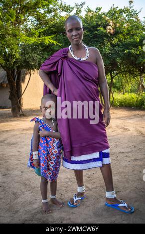 Eine Maasai-Frau in traditioneller Kleidung steht mit ihrem kleinen Sohn im Dorf Mikumi, Tansania. Stockfoto