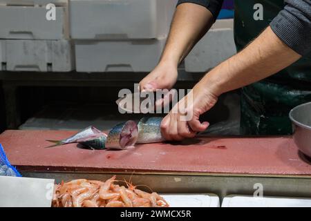 Nahaufnahme von Männerhänden, die Fische mit einem Messer am Tisch schneiden Stockfoto