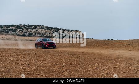 Rotes modernes Auto, das auf einer unbefestigten Wüstenstraße in einer Staubwolke fährt, Cape Greco Nationalpark in Zypern Stockfoto