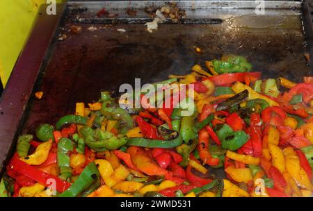 Gelbe rote und grüne Paprika brutzeln auf der heißen Grillplatte eines Street Food Trucks, der mit Gewürzen kocht Stockfoto