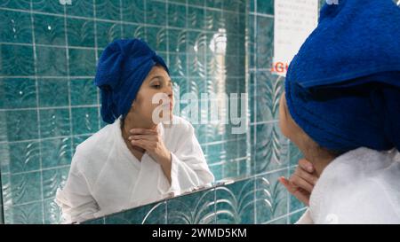 Eine junge Frau im Badezimmer massiert ihren Hals vor dem Spiegel Stockfoto
