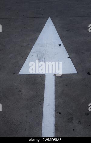 Ein weißer Pfeil auf grauem Asphalt weist auf Vorwärtsbewegung hin und triumphiert Stockfoto