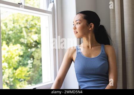 Eine junge Frau aus der Rasse schaut zu Hause aus dem Fenster Stockfoto