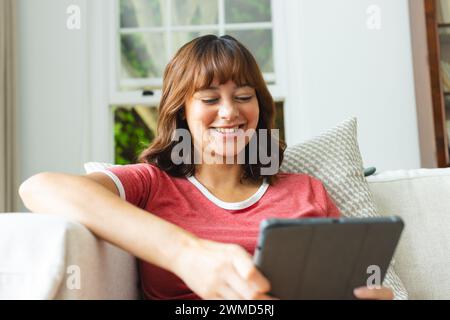 Eine junge birassische Frau lächelt, während sie zu Hause ein Tablet benutzt Stockfoto