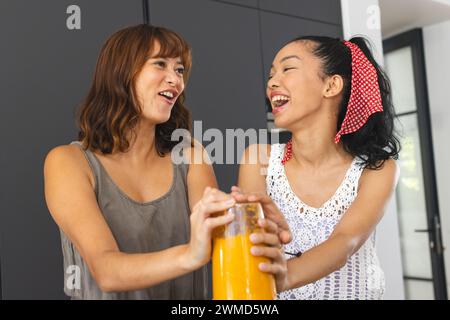 Birassische Freundinnen teilen einen fröhlichen Moment in der Küche und machen Smoothies Stockfoto