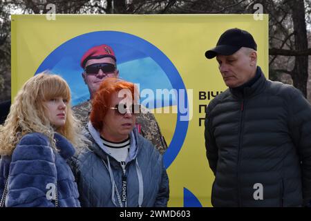 Verwandte sind neben dem Stand eines Porträts eines gefallenen ukrainischen Soldaten im Zentrum von Zaporischschschiha zu sehen. Der ukrainische Präsident Wolodymyr Zelenski hat den zweiten Jahrestag der russischen Invasion begangen, indem er sagte, dass sein Land "erfolgreich sein wird". Die Ukraine widersetzte sich den Prognosen, Russland zu bekämpfen, aber es gibt Anzeichen dafür, dass sich der Krieg zu Gunsten Russlands wendet. Die ukrainische Regierung hat längst aufgehört, die Zahl ihrer Toten zu teilen. Aber die ständig wachsende Zahl frischer Gräber auf beiden Seiten der Frontlinie zeichnet ein schmerzhaft klares Bild. Stockfoto