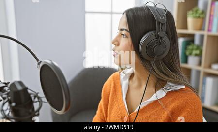 Junge hispanische Frau, die Kopfhörer trägt und in einem professionellen Studio in ein Mikrofon spricht. Stockfoto