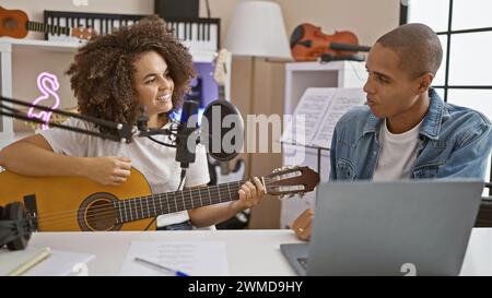 Zwei Künstler spielen klassische Melodien auf klassischer Gitarre, singen lächelnd mit Laptop im Musikstudio, eine Mischung aus klassisch und digital Stockfoto